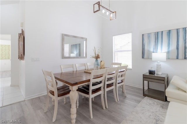 dining room with a high ceiling, a notable chandelier, a wealth of natural light, and light hardwood / wood-style flooring