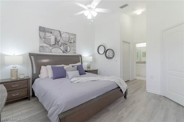 bedroom with a towering ceiling, ceiling fan, ensuite bathroom, and light wood-type flooring