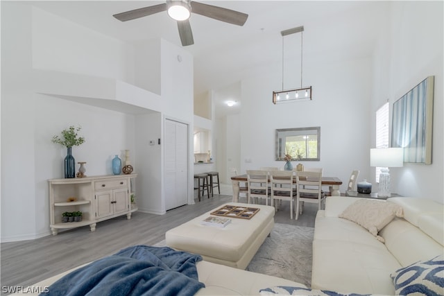 living room with a towering ceiling, ceiling fan with notable chandelier, and light hardwood / wood-style flooring