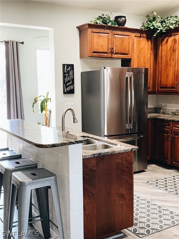 kitchen featuring a kitchen bar, light hardwood / wood-style flooring, dark stone counters, stainless steel fridge, and sink