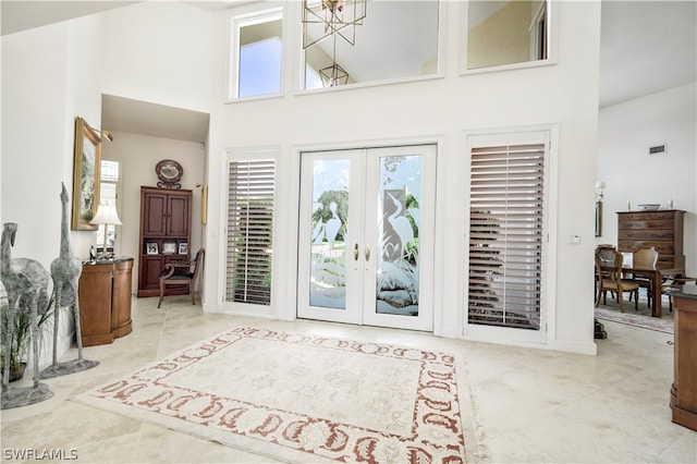 foyer entrance with french doors, high vaulted ceiling, a chandelier, and light tile patterned floors