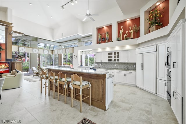 kitchen featuring light stone countertops, a center island, a high ceiling, decorative backsplash, and white cabinets