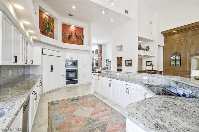 kitchen with light stone countertops, a towering ceiling, white cabinetry, and black appliances