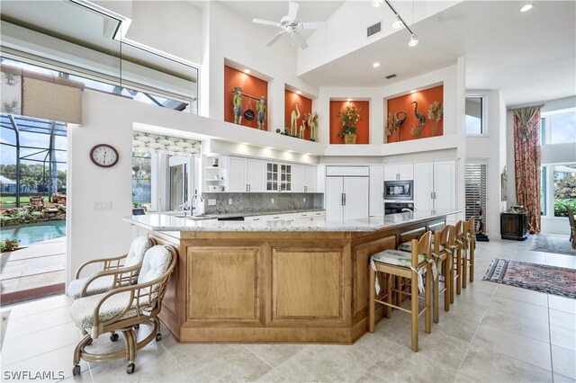 kitchen featuring high vaulted ceiling, white cabinets, built in appliances, ceiling fan, and light stone countertops