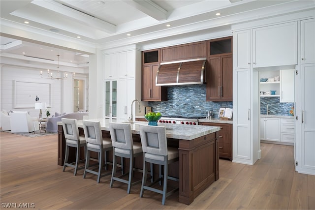 kitchen with an island with sink, extractor fan, light countertops, light wood-style floors, and beam ceiling