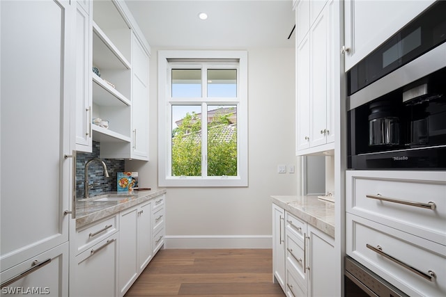 kitchen featuring wood finished floors, a sink, white cabinetry, baseboards, and tasteful backsplash