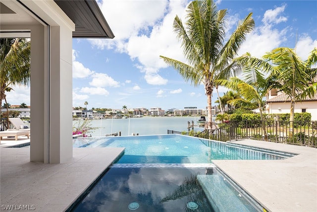 view of swimming pool featuring a water view, fence, and a pool with connected hot tub