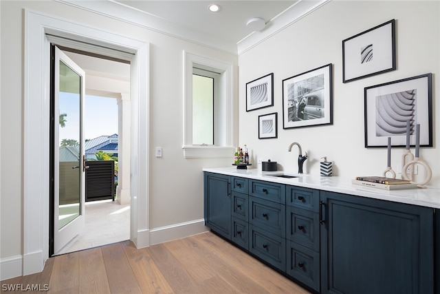 bar with crown molding, a sink, light wood-style flooring, and baseboards