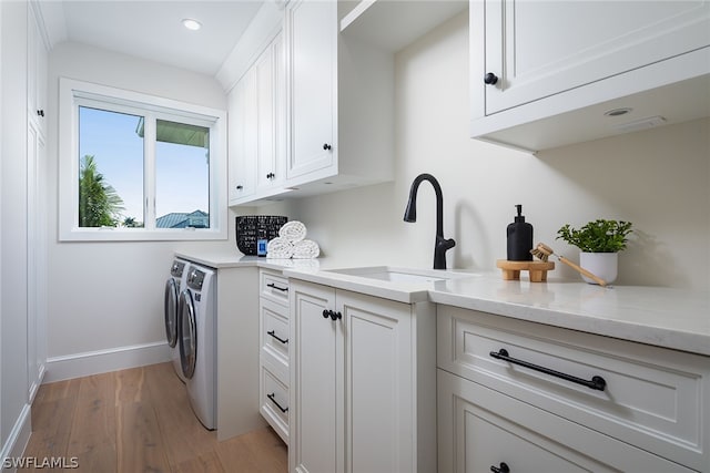 washroom featuring light wood-style flooring, a sink, baseboards, independent washer and dryer, and cabinet space