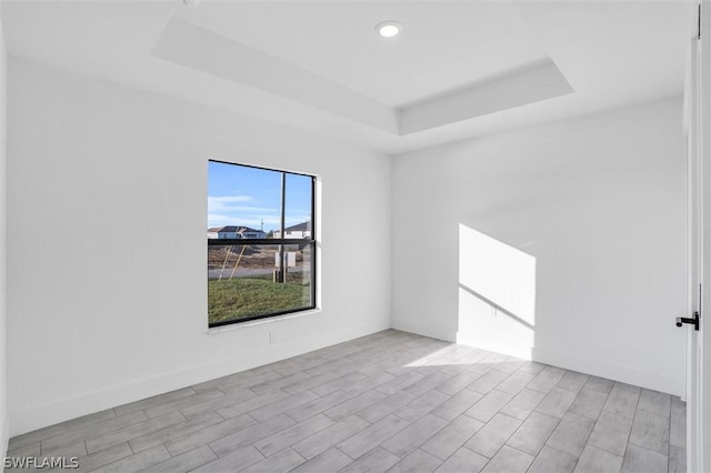 spare room featuring a tray ceiling, baseboards, and wood finished floors