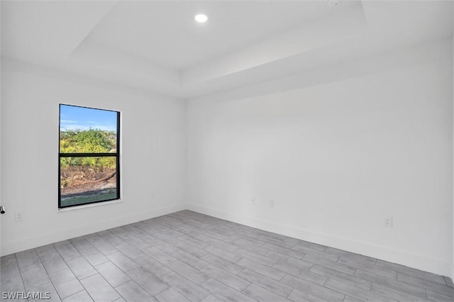 spare room featuring a raised ceiling, wood finished floors, recessed lighting, and baseboards