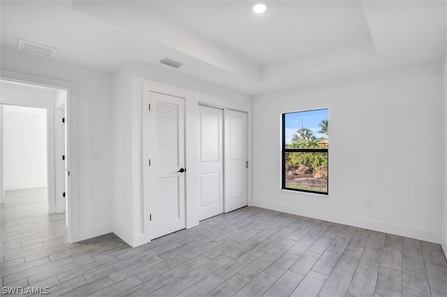 unfurnished bedroom with a tray ceiling, baseboards, visible vents, and wood finished floors