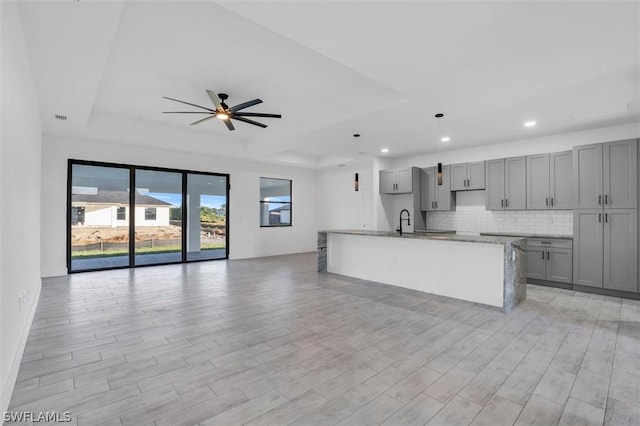 kitchen with a tray ceiling, gray cabinetry, open floor plan, and decorative backsplash