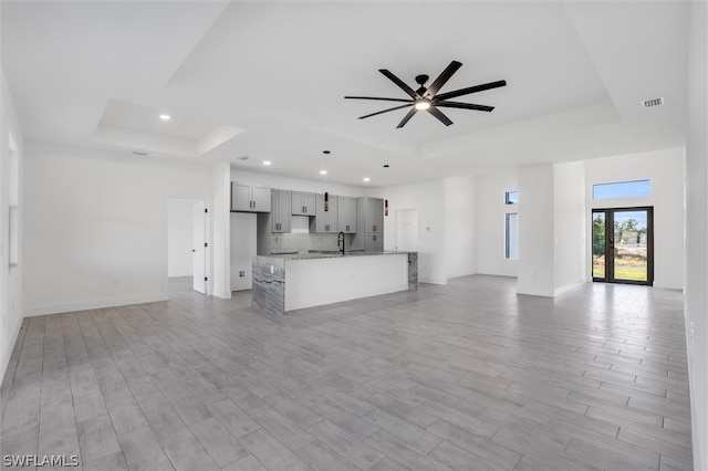 unfurnished living room featuring a tray ceiling, ceiling fan, and light hardwood / wood-style floors