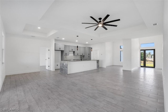 unfurnished living room with a sink, a tray ceiling, and light wood-style flooring