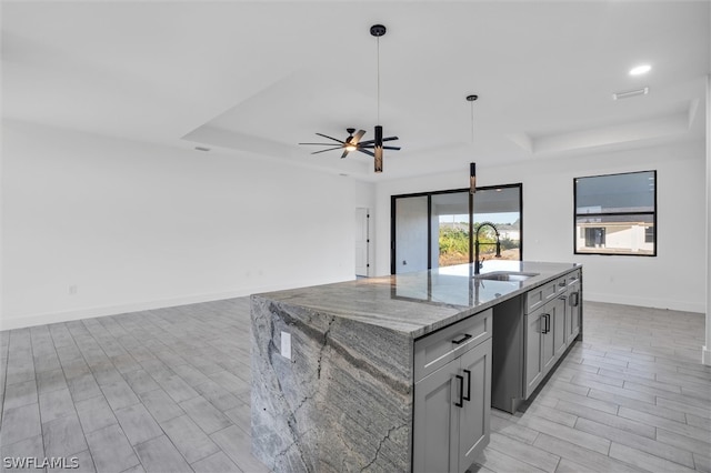 kitchen with light stone countertops, sink, decorative light fixtures, a center island with sink, and light hardwood / wood-style floors