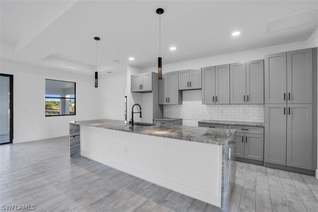 kitchen featuring a sink, backsplash, a kitchen island with sink, and gray cabinets