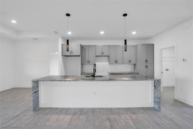 kitchen with light hardwood / wood-style floors, hanging light fixtures, dark stone counters, and sink