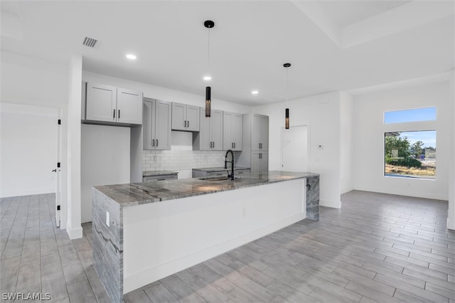 kitchen with sink, dark stone countertops, light wood-type flooring, and hanging light fixtures