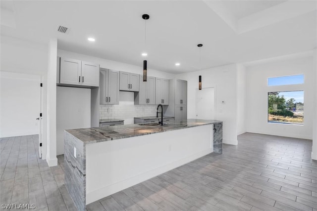 kitchen with visible vents, stone countertops, gray cabinets, a sink, and tasteful backsplash