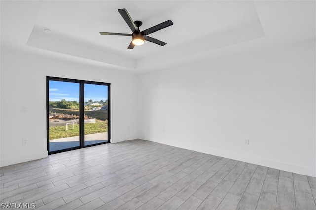 spare room with ceiling fan, light hardwood / wood-style floors, and a tray ceiling