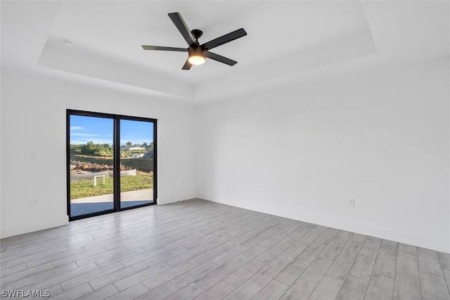 spare room featuring a raised ceiling, ceiling fan, and wood finished floors