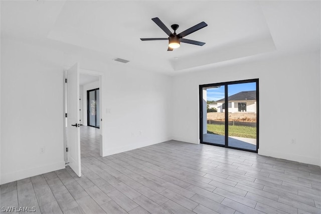 empty room with a ceiling fan, wood finished floors, visible vents, baseboards, and a tray ceiling