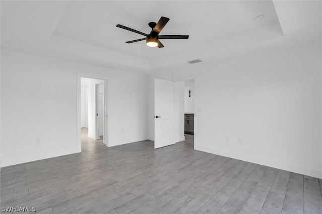 unfurnished room with ceiling fan, light hardwood / wood-style floors, and a tray ceiling