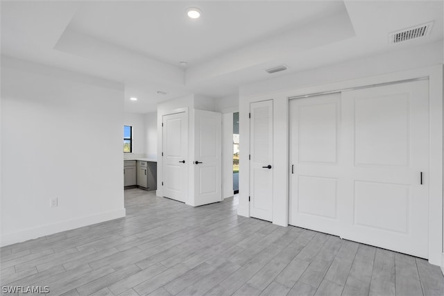 unfurnished bedroom featuring connected bathroom, light hardwood / wood-style floors, and a tray ceiling