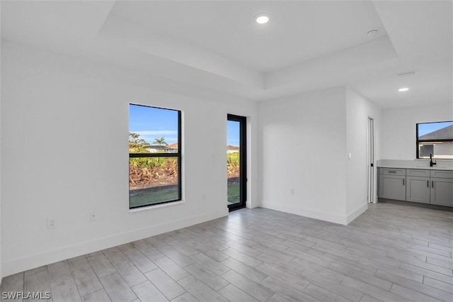 unfurnished room with light wood-style floors, recessed lighting, a raised ceiling, and baseboards