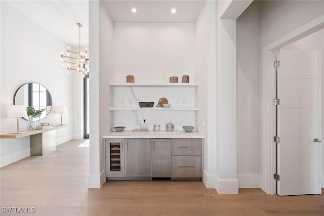 bar featuring light wood finished floors, baseboards, an inviting chandelier, and decorative light fixtures