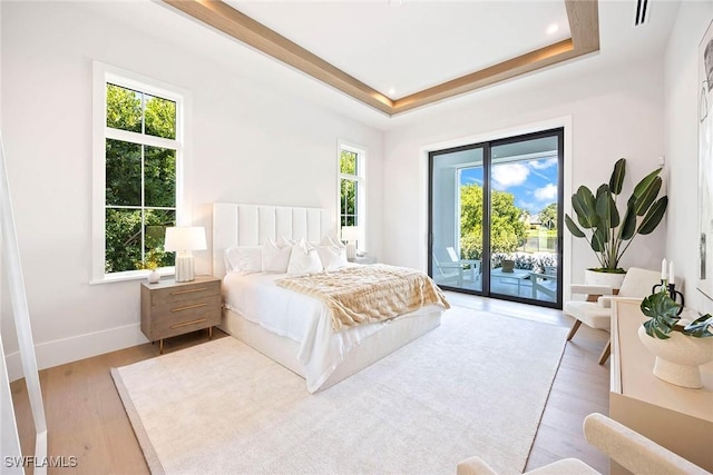 bedroom featuring access to outside, multiple windows, a tray ceiling, and light wood-style flooring