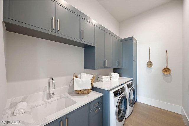 laundry area featuring cabinet space, baseboards, light wood-style flooring, independent washer and dryer, and a sink