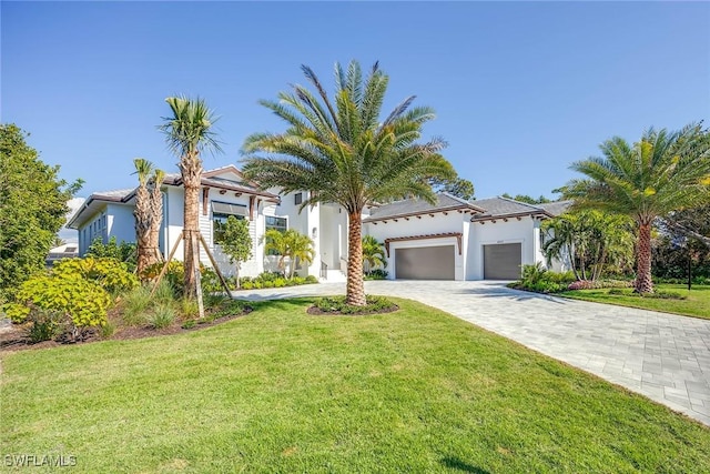 mediterranean / spanish home featuring a front lawn, decorative driveway, an attached garage, and stucco siding