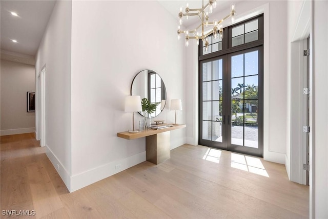 doorway with light wood finished floors, a high ceiling, baseboards, and french doors