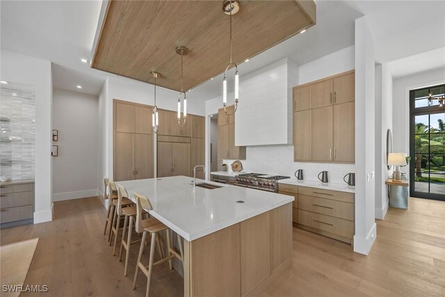 kitchen featuring a kitchen island with sink, a sink, light countertops, hanging light fixtures, and double oven range