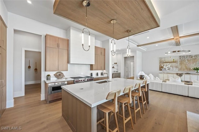 kitchen featuring light wood-style flooring, a center island with sink, pendant lighting, and a sink