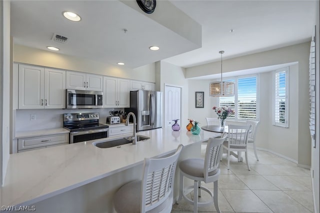 kitchen featuring stainless steel appliances, decorative light fixtures, a breakfast bar area, white cabinets, and sink