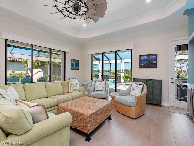 living room with ornamental molding, a healthy amount of sunlight, light wood-type flooring, and a tray ceiling