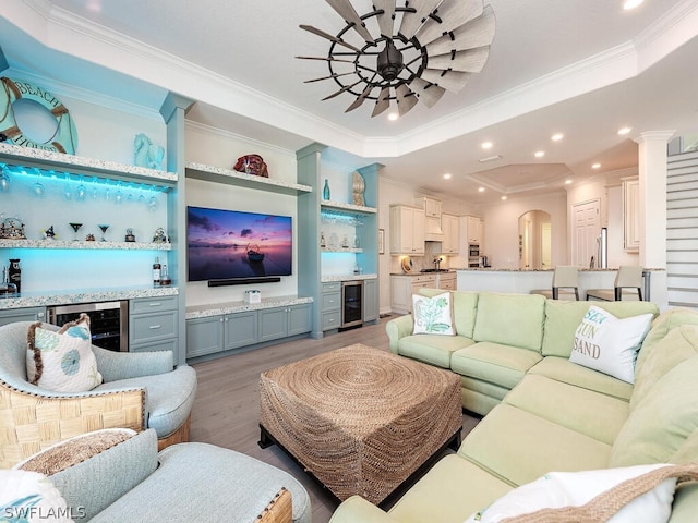 living room with light hardwood / wood-style flooring, crown molding, a raised ceiling, and beverage cooler