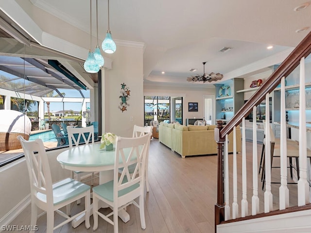 dining area featuring crown molding, an inviting chandelier, a tray ceiling, and light hardwood / wood-style flooring