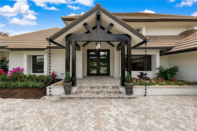 property entrance featuring a tile roof, french doors, and stucco siding