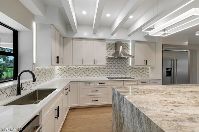 kitchen featuring wall chimney range hood, stainless steel appliances, sink, white cabinetry, and light stone counters