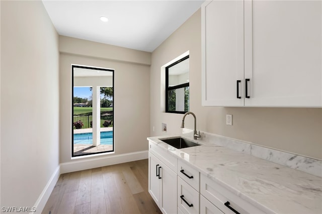 kitchen with light wood-type flooring, plenty of natural light, a sink, and light stone countertops