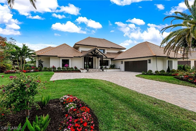 view of front facade with a front yard, decorative driveway, a tile roof, and an attached garage