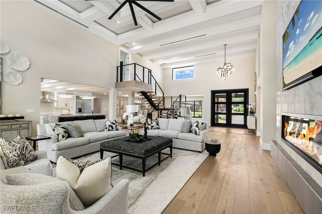 living room featuring beamed ceiling, a tile fireplace, light hardwood / wood-style flooring, and a towering ceiling