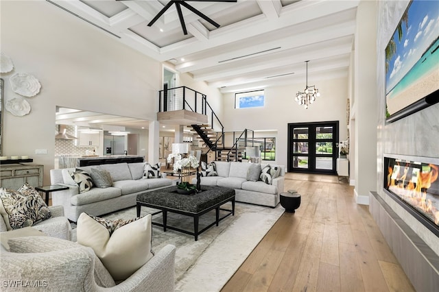 living area featuring stairway, a high ceiling, a tiled fireplace, light wood-style floors, and beamed ceiling