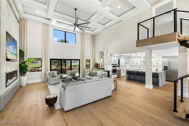 living room featuring ceiling fan, light hardwood / wood-style flooring, beamed ceiling, a towering ceiling, and coffered ceiling