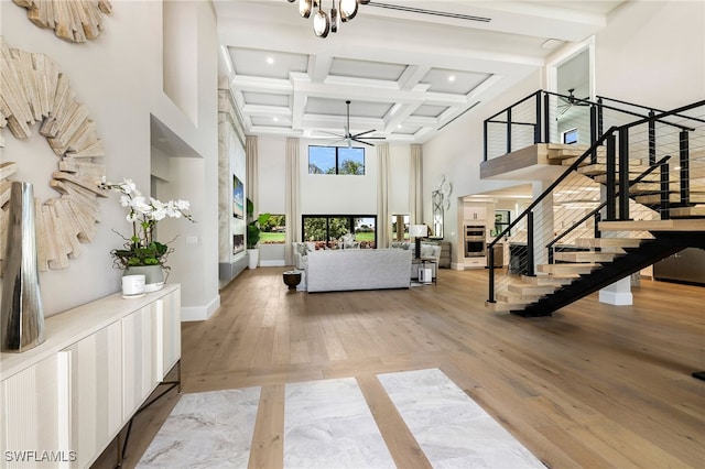 interior space with coffered ceiling, light wood-style flooring, a high ceiling, and stairs