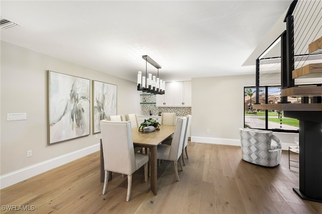 dining area featuring light wood-type flooring, baseboards, visible vents, and a notable chandelier